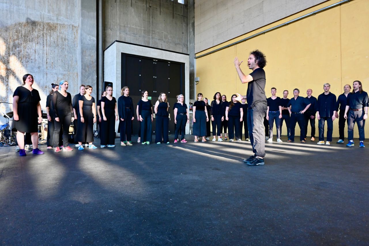 Der Vivo Chor singt, alle tragen schwarze Kleidung. Im Vordergrund Chorleiter Beat Vögele. 